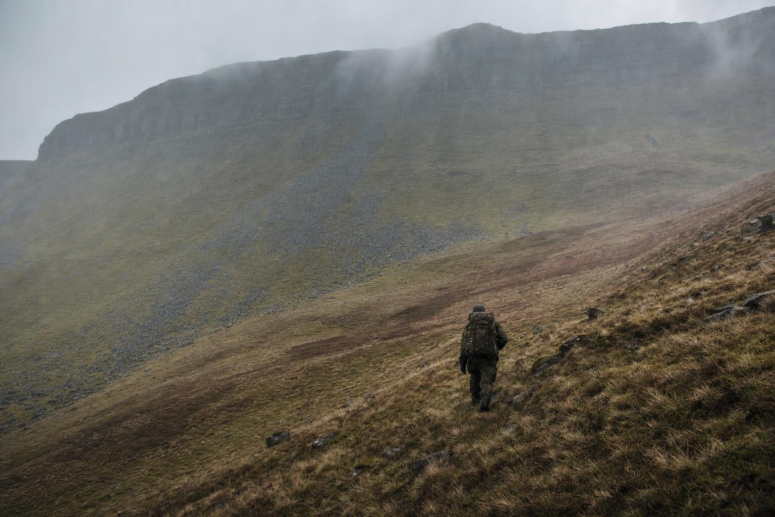 A lone soldier carrying a heavy bergen up a mountain ridge in the Brecon Beacons