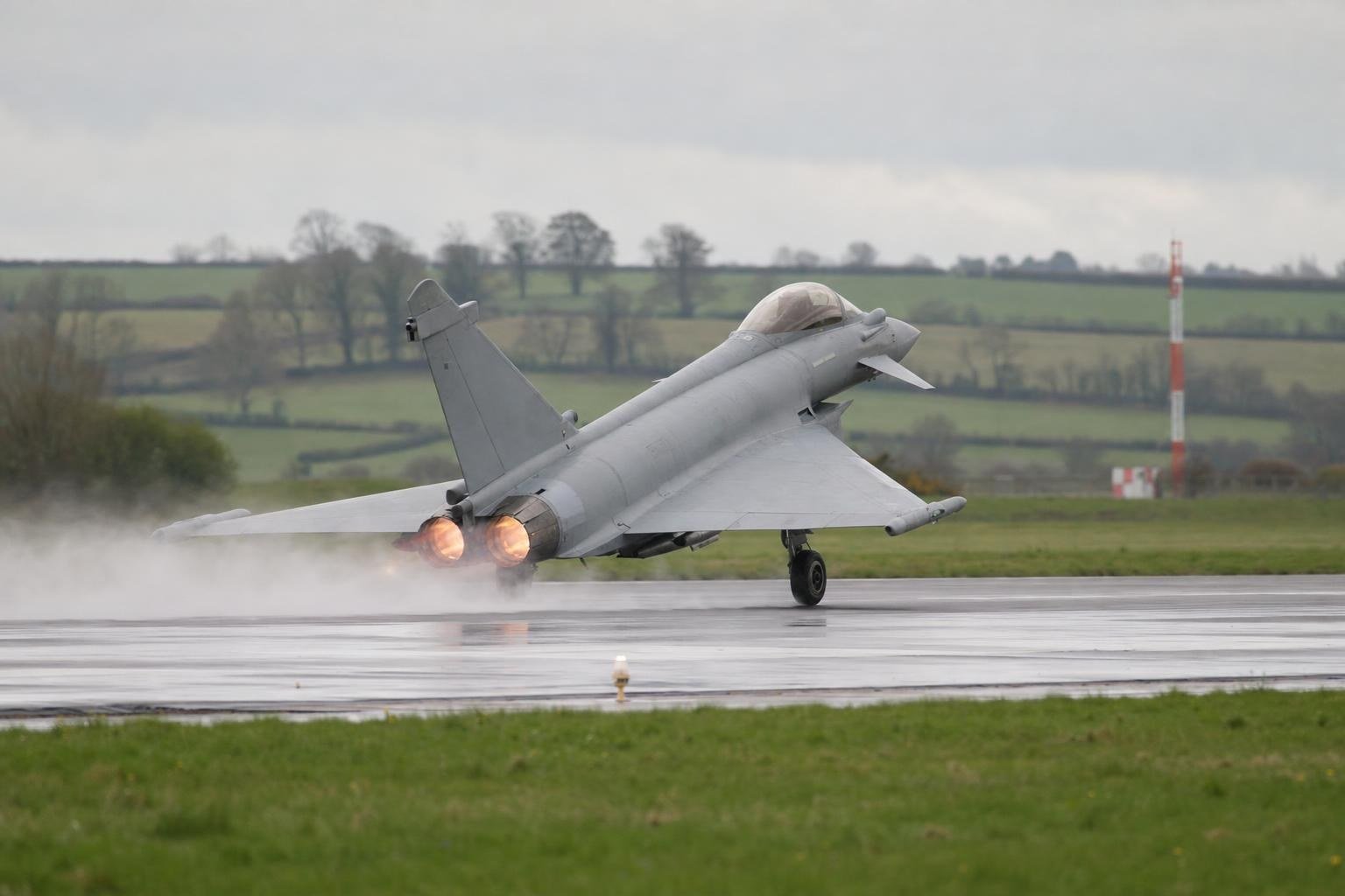 A delta-wing fighter jet with canards taking off from a wet British runway